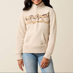 10079247 Ariat Girls Running Wild Qtr Zip at. boltranchstore.com in stock free shipping A young girl smiling and wearing a cream-colored quarter-zip sweatshirt with a graphic of horses across the chest