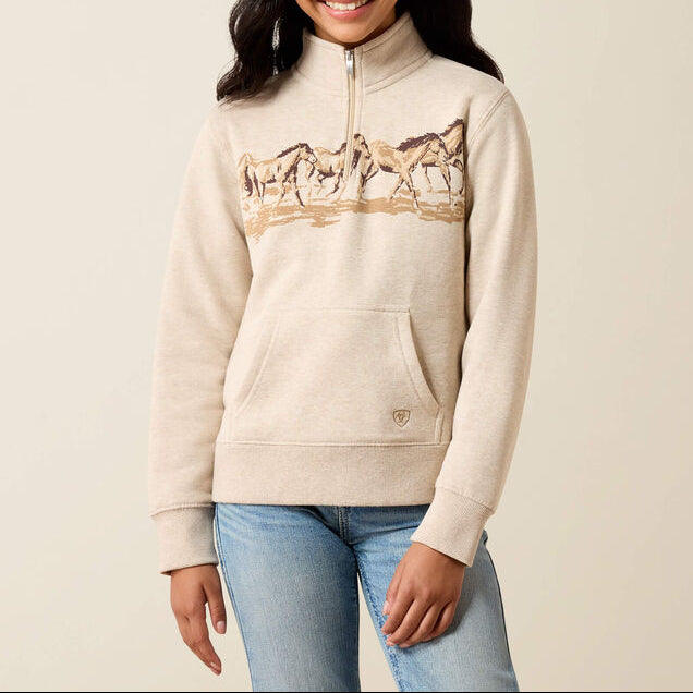 10079247 Ariat Girls Running Wild Qtr Zip at. boltranchstore.com in stock free shipping A young girl smiling and wearing a cream-colored quarter-zip sweatshirt with a graphic of horses across the chest