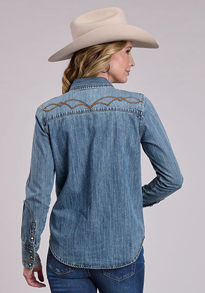 Woman wearing a blue denim shirt with decorative stitching and a beige cowboy hat on a light gray background