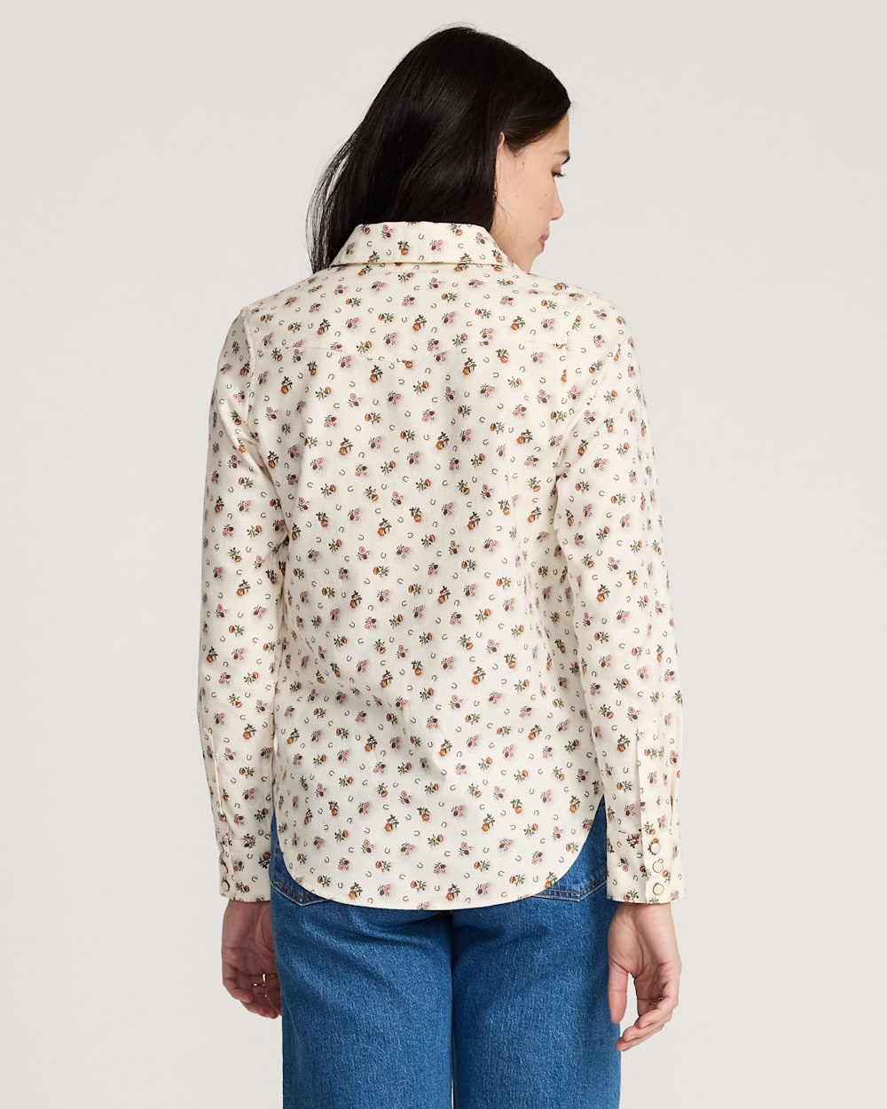 Woman wearing a floral patterned shirt and blue jeans on a plain background