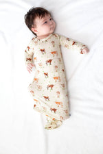 Baby lying on a white blanket wearing a long-sleeve onesie with animal prints. Longhorn Cows Knotted Infant Gown shop today at boltranchstore.com