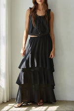 Woman wearing a black layered skirt and top against a white wall.