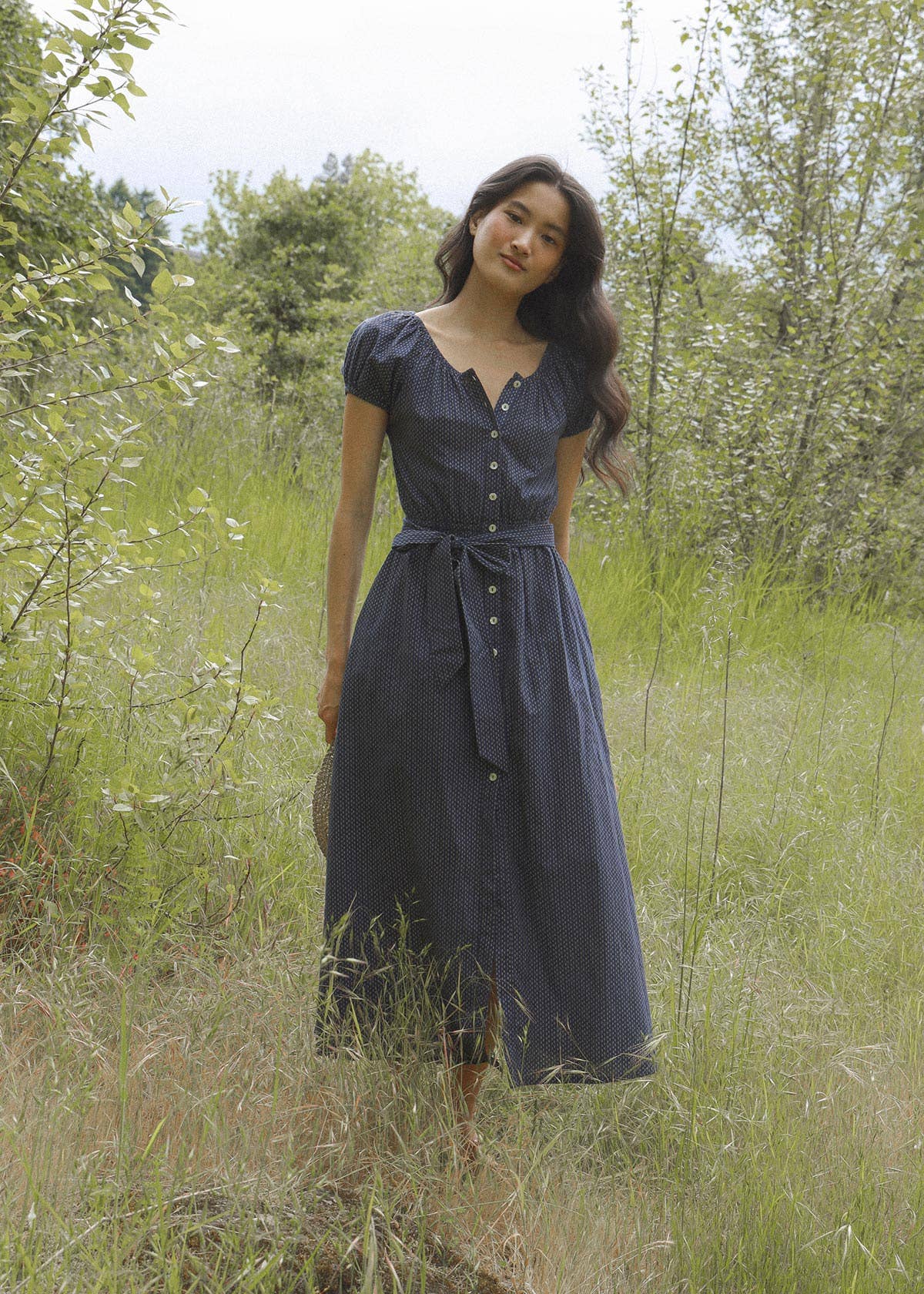 Woman in a blue dress standing in a grassy field with trees in the background doen dupe boltranchstore.com Bolt Ranch Store blue polka dot dress