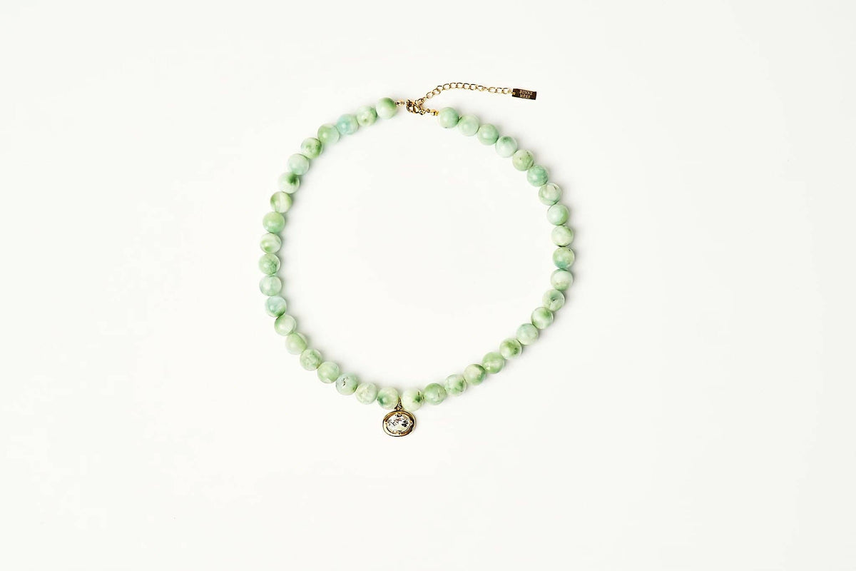 A beaded necklace made of light green marbled beads with a small gold-tone pendant and extender chain, displayed on a clean white background. shop at boltranchstore.com