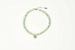 A beaded necklace made of light green marbled beads with a small gold-tone pendant and extender chain, displayed on a clean white background. shop at boltranchstore.com