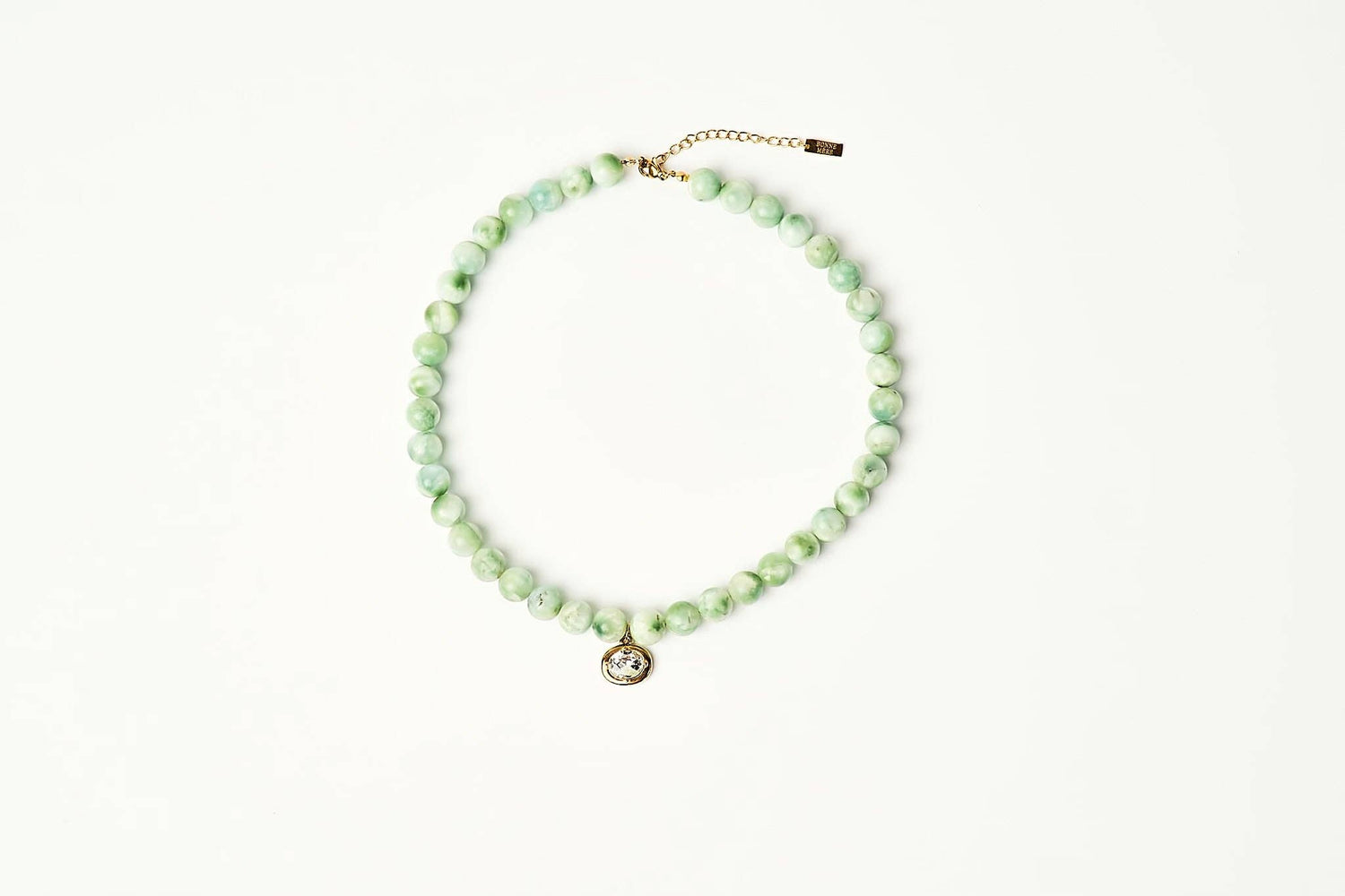 A beaded necklace made of light green marbled beads with a small gold-tone pendant and extender chain, displayed on a clean white background. shop at boltranchstore.com