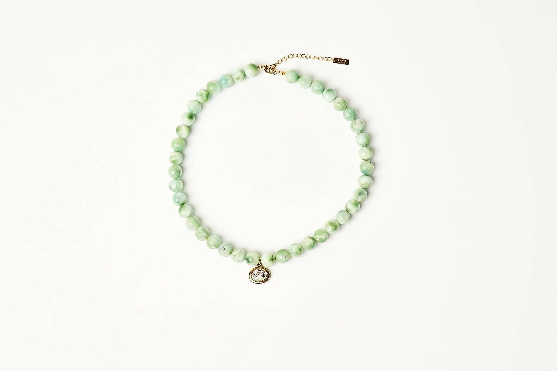A beaded necklace made of light green marbled beads with a small gold-tone pendant and extender chain, displayed on a clean white background. shop at boltranchstore.com