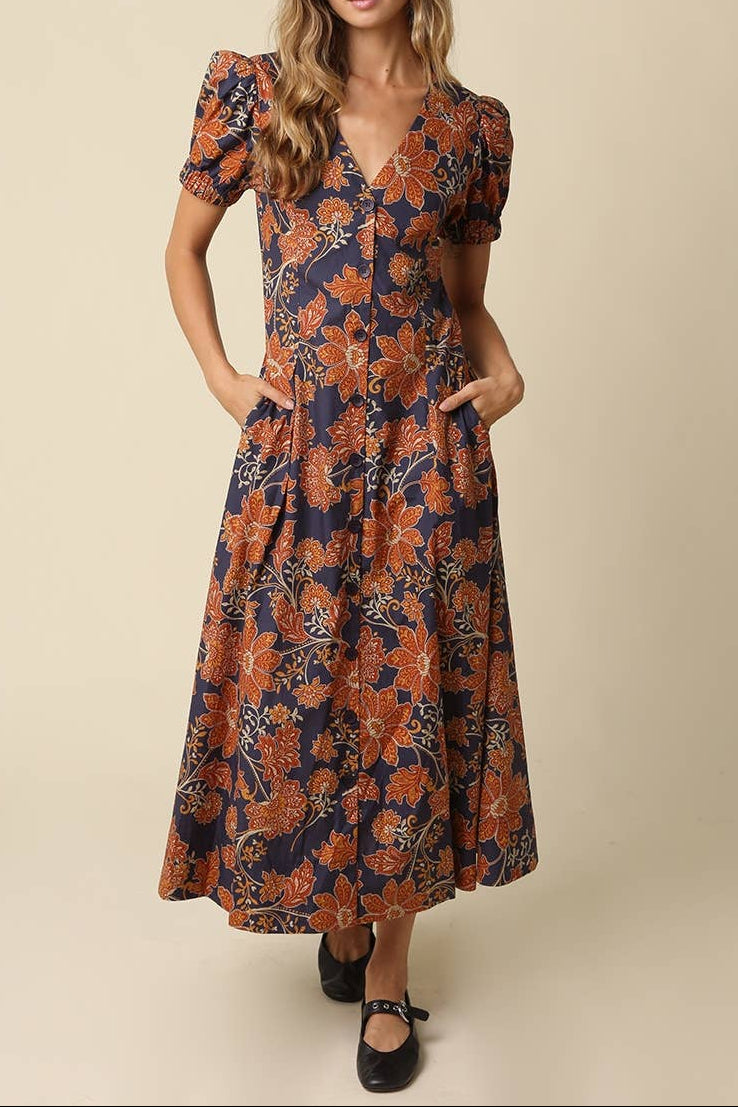 Hallie Floral V Neck Maxi Dress. navy blue midi dress with a rust-orange floral pattern with short puff sleeves, and a V-neckline. Find at bolt ranch store
