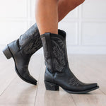 Lane Sandaga Midi Boot in Jet Black at boltranchhstore.com in stock free shipping Black cowboy boots with floral embroidery worn by a person on a light wooden floor.