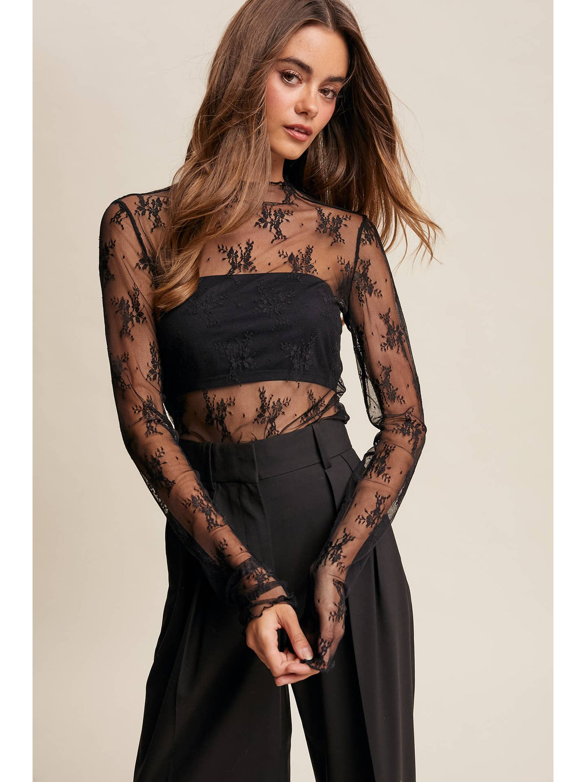 A black sheer floral lace long-sleeve crop top with a bandeau-style neckline with a lace detail throughout the top
