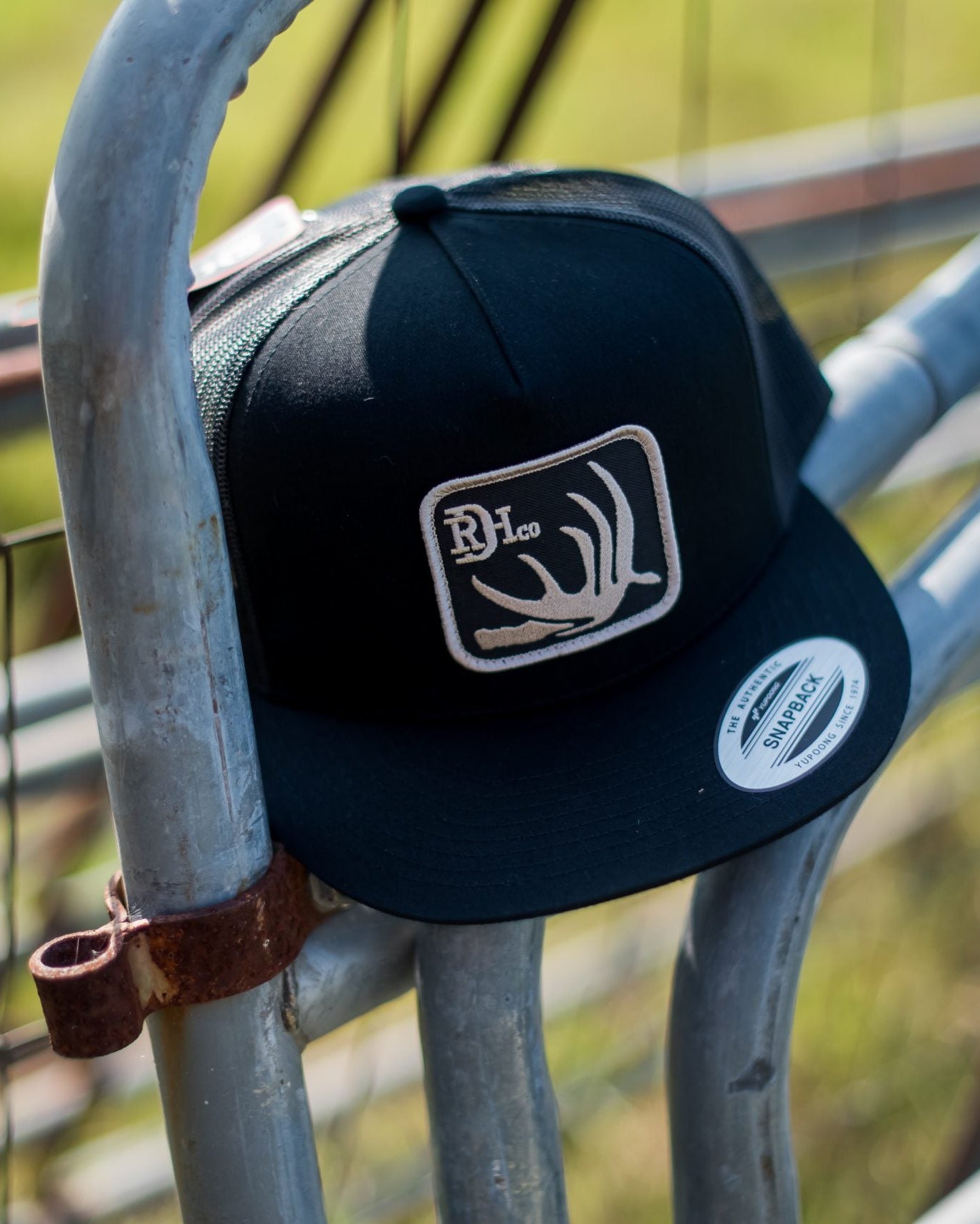 Red Dirt Hat features a deer antler patch on a black hat with black mesh back in a flat bill and snap back hat available at boltranchstore.com