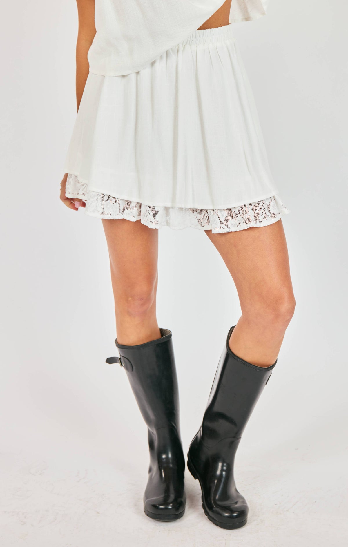 Person wearing a white dress with lace trim and black rain boots on a white background Sammy Lace Mini Skirt DOEN DUPE
