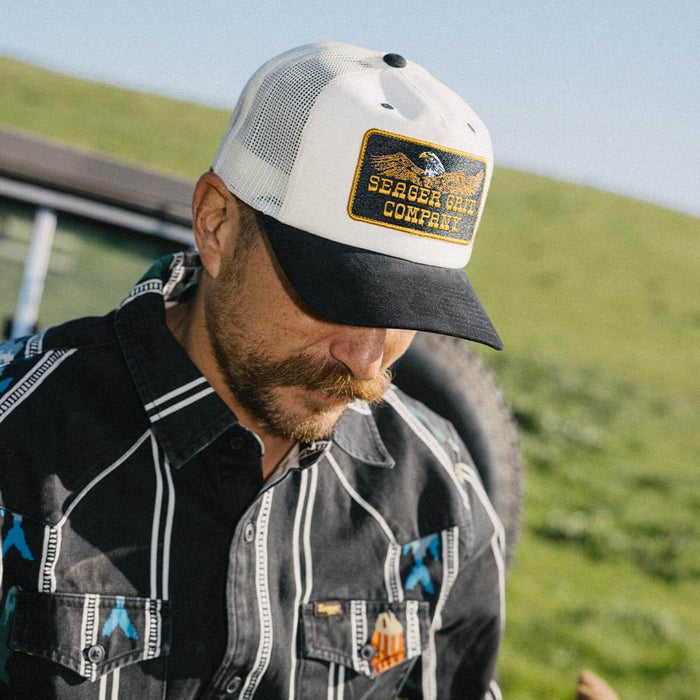 Seager Big Rig Trucker Snapback At boltranchstore.com in stock free shipping A man wearing a white and black trucker hat with a 'Seeger Gold Company' embroidered patch on the front
