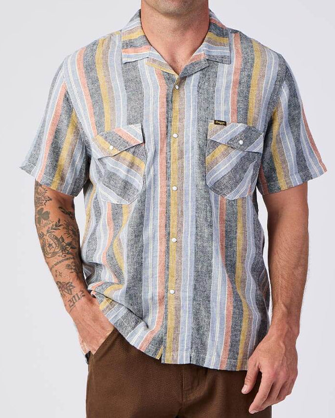 Seager Whippersnapper Shirt Men's short-sleeve snap-front camp shirt featuring a vertical stripe pattern in charcoal gray, light blue, mustard yellow, and muted coral. The relaxed-fit shirt has a spread collar, two snap-flap chest pockets with diagonal stripe placement, and a lightweight textured fabric available at boltranchstore.com