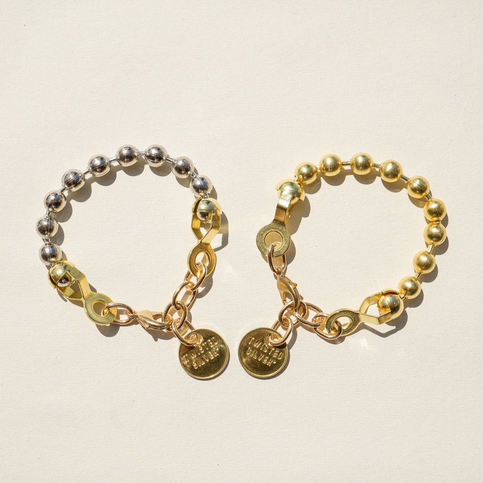 Twisted Silver Ball And Chain Bracelet at boltranchstore.com free shipping in stock Two beaded bracelets on a light beige background. One bracelet is metallic silver with gold-toned chain links and round charms, and the other is gold-toned with silver-toned chain links and round charms.
