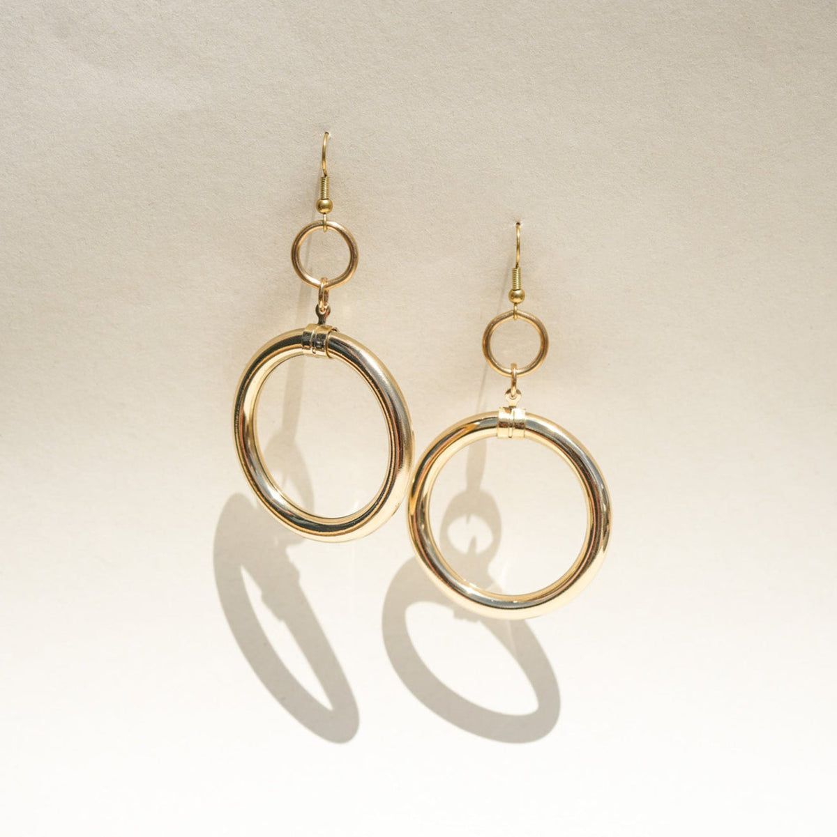 A pair of gold-tone dangle earrings with a large open circular hoop and a smaller top ring.