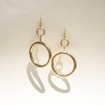 A pair of gold-tone dangle earrings with a large open circular hoop and a smaller top ring.