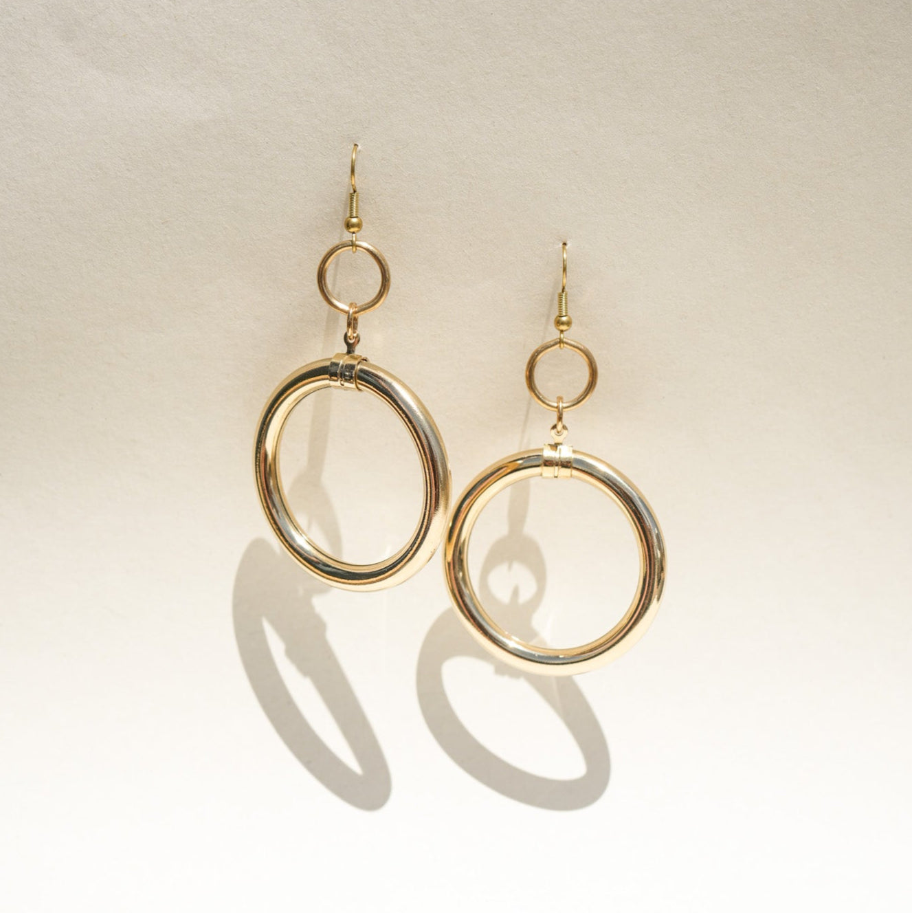 A pair of gold-tone dangle earrings with a large open circular hoop and a smaller top ring.