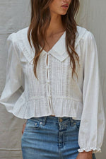 Woman wearing a white blouse with long sleeves and blue jeans against a neutral background