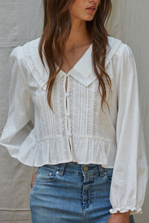 Woman wearing a white blouse with long sleeves and blue jeans against a neutral background