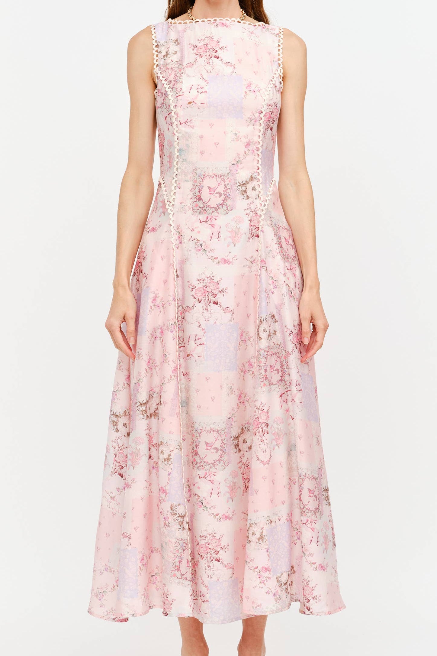 A woman modeling a sleeveless midi dress with a pink and white floral pattern, lace trim at the neckline and waist, and a flared skirt, set against a plain white studio background. Shop today at boltranchstore.com