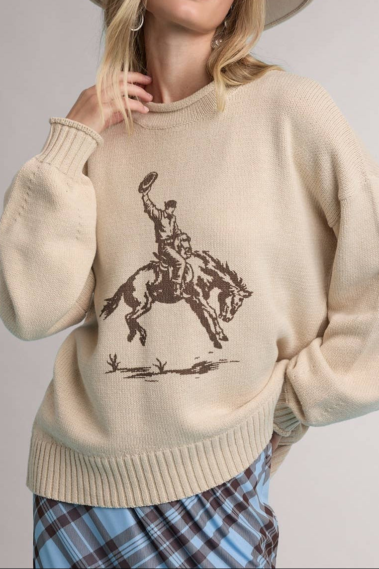 Woman wearing a beige sweater with a graphic design, glasses, and a hat on a light gray background Loretta sweater shop today at boltrachstore.com