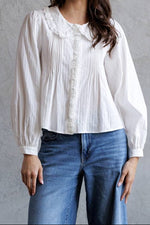 Woman wearing a white blouse and blue jeans against a gray wall.