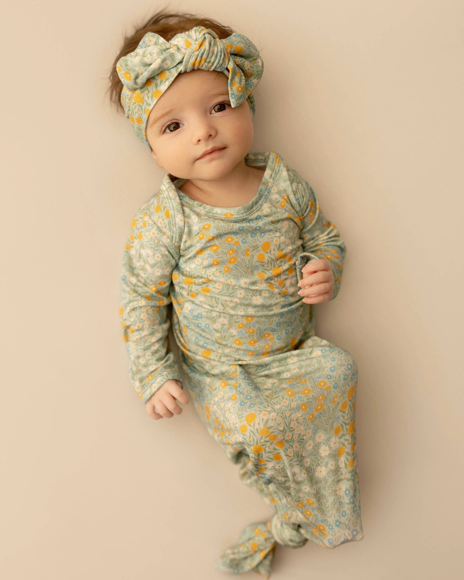 Baby in floral outfit and headband on a beige background Blue Meadows Knotted Infant Gown Shop today at boltranchstore.com 
